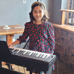 Picture of a young piano student. This student is enrolled in our kids piano lessons program. Her piano teacher was very proud of her and you can tell by her smile that she knows she played the piano very well. 